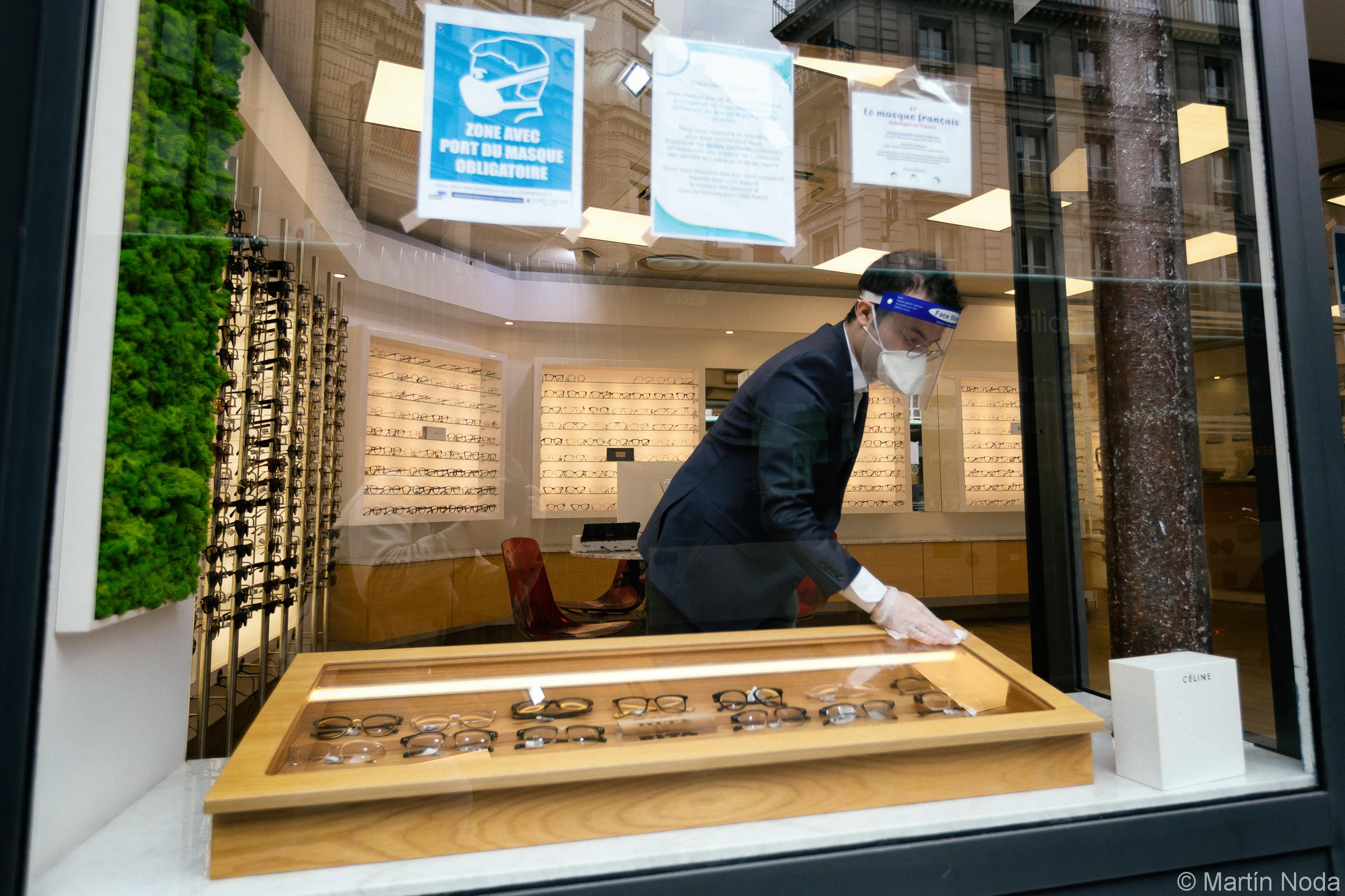 Un opticien, portant une masque, une visiere et des gants, nettoie la vitrine en vue de l ouverture du magasin, Paris, 11 mai 2020.